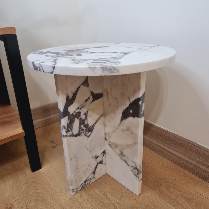 May include: A round white marble side table with a unique, veined pattern. The table has a circular top and a base with a geometric design.