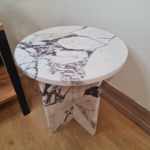 May include: A round white marble table with a white marble base. The table has a unique veined pattern in shades of pink and gray.