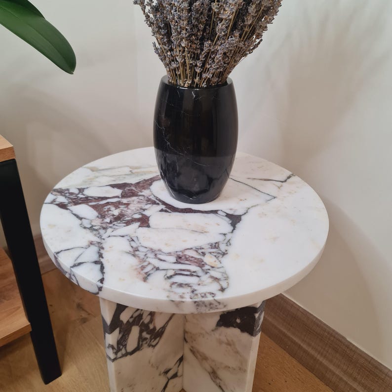 May include: A round marble side table with a white and pink marble top and a black marble vase with dried lavender flowers on top.