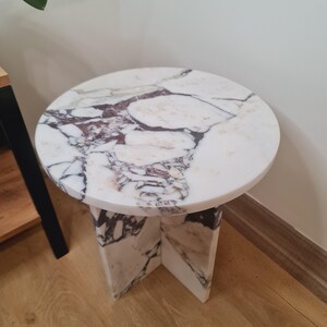 May include: A round white marble side table with a unique veined pattern. The table has a simple, modern design with a circular top and a square base.