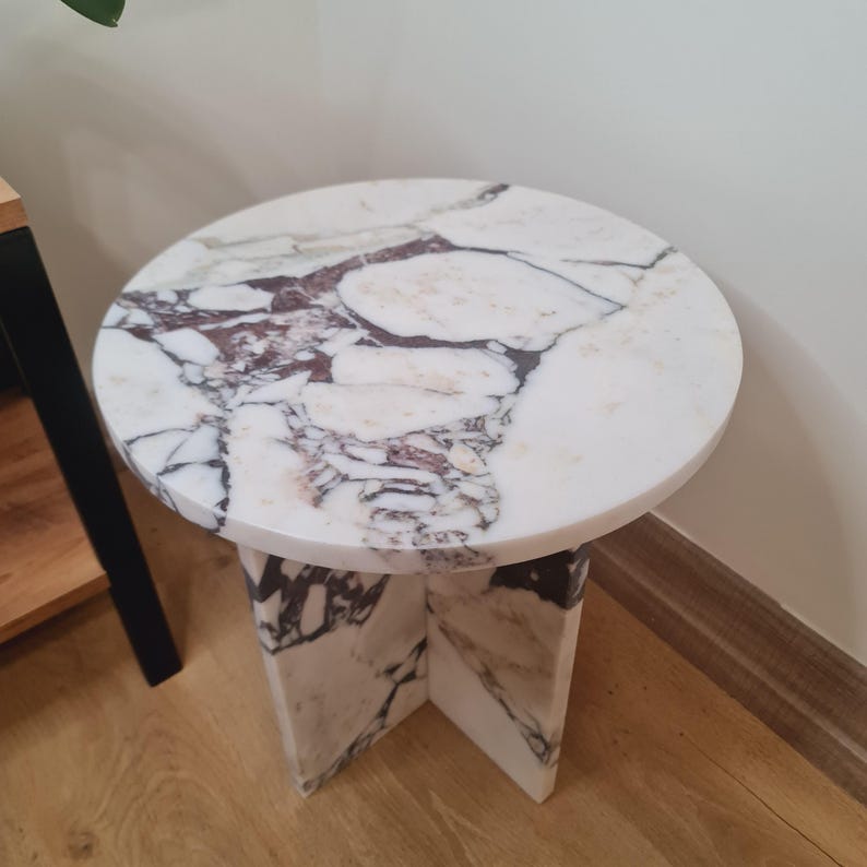 May include: A round white marble side table with a unique veined pattern. The table has a simple, modern design with a circular top and a square base.