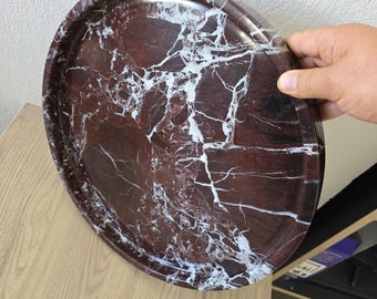 Op de afbeelding: Een rond dienblad met een dieproodbruine basis en opvallende witte aders over het gehele oppervlak. Het dienblad heeft een gladde, gepolijste afwerking en een opstaande rand, wat zorgt voor een uiterlijk dat lijkt op natuursteen.