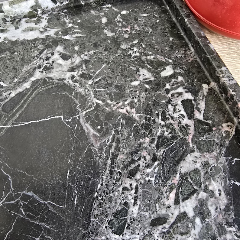 Op de afbeelding: Een rechthoekig dienblad met een donkerzwart stenen oppervlak met ingewikkelde witte en grijze aders. Het dienblad heeft een opstaande rand en een gepolijste afwerking, wat een natuurlijke marmertextuur met hoekige steenfragmenten toont.