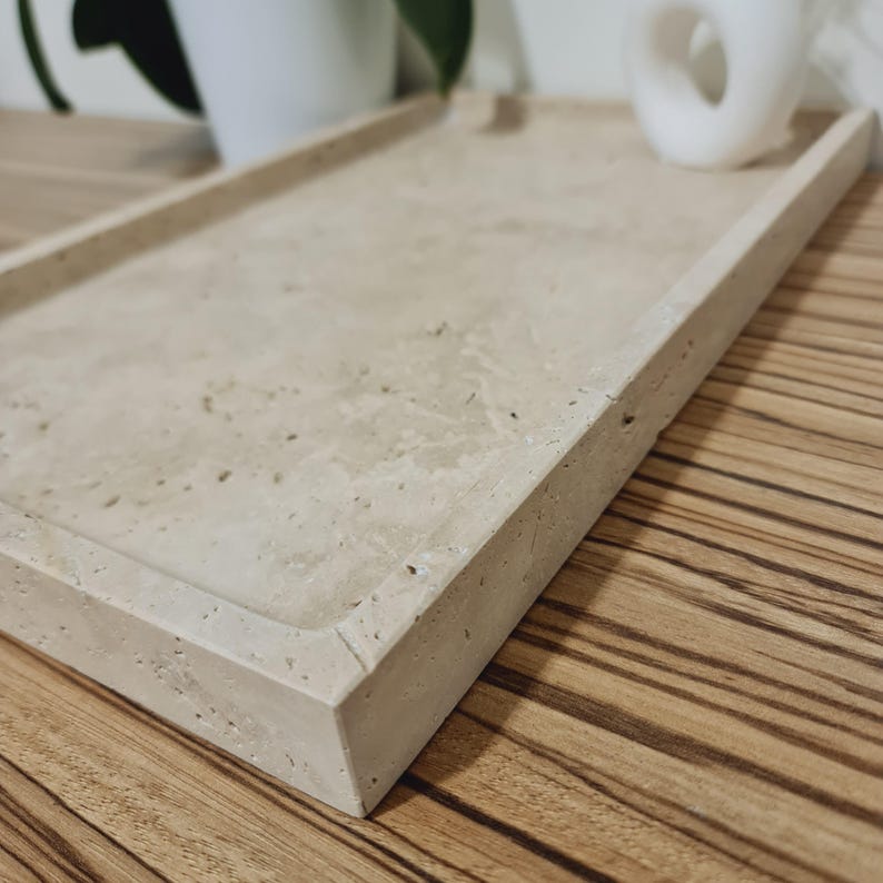 Puede incluir: Una bandeja rectangular de color beige con una superficie ligeramente texturizada y bordes elevados. La bandeja tiene un dise&ntilde;o minimalista y est&aacute; hecha de un material similar a la piedra. Adecuada para servir o exhibir. Mide aproximadamente 30 cm de largo y 20 cm de ancho.