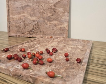 May include: Two rectangular, marble trays with a reddish-brown hue. The trays have a raised edge and are filled with red rose hips. The trays are on a wooden surface.