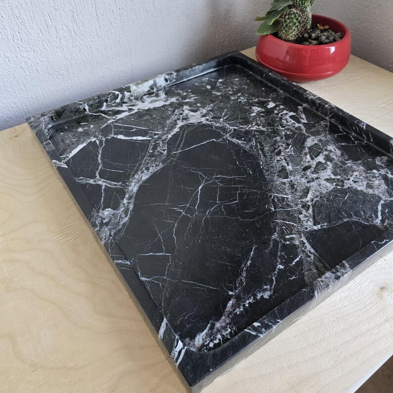 Op de afbeelding: Een rechthoekig dienblad van zwart marmer met opvallende witte aders over het gehele oppervlak. Het dienblad heeft een opstaande rand en een gladde, gepolijste afwerking, waarbij het natuurlijke steenpatroon met diepzwarte tinten wordt getoond.