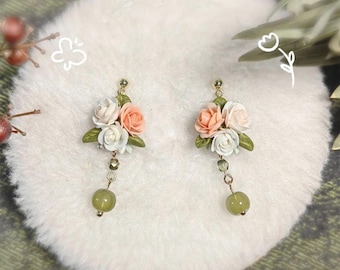 May include: A pair of floral dangle earrings with three white and peach colored polymer clay flowers on each earring. The earrings have a gold tone and a green stone dangle.