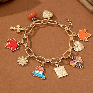 May include: A gold charm bracelet with various autumn-themed charms, including a pumpkin, a car, a turkey, a heart, a leaf, a cross, and a book. The charms are all brightly colored and have a glossy finish.