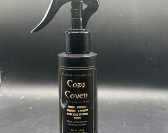 Peut inclure: Flacon pulvérisateur noir avec une buse noire. L'étiquette indique "Cozy Coven Room and Linen Spray" avec des notes de parfum. La bouteille contient 118 ml de produit. Fabriqué aux États-Unis.