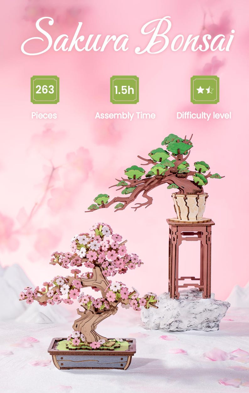 May include: Two wooden 3D puzzles of cherry blossom bonsai trees. The larger tree has green leaves and is on a stand. The smaller tree has pink blossoms and is in a pot. Both trees are on a white surface with pink flower petals.