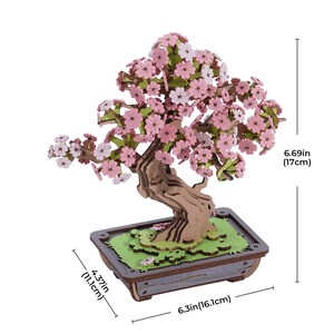 May include: A wooden 3D model of a cherry blossom bonsai tree with pink flowers. The tree is 6.69 inches tall and 6.3 inches wide. The base of the tree is a wooden pot with a green and brown design.