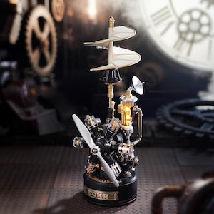Może przedstawiać: Dekoracyjna lampa w stylu steampunk z czarną podstawą i skomplikowanymi metalowymi elementami. Posiada śmigło, podwójną spiralę i świecący element świetlny. Na podstawie napis "ROKR". Unikalny przedmiot dekoracyjny.
