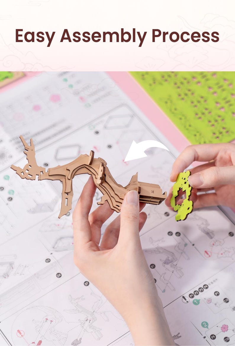 May include: A person assembling a wooden model of a tree with detailed instructions. The model is made of brown wood and has a green leaf design. The person is holding the model in their left hand and a green leaf piece in their right hand.