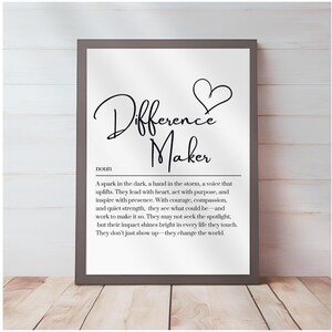 May include: A framed print with the words "Difference Maker" in elegant script, accompanied by a heart symbol. The print includes a definition of the term, all in black text on a white background, framed in a gray border.