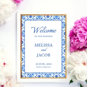 Peut inclure: Une pancarte de bienvenue blanche avec une bordure bleue et dorée. La pancarte indique "Bienvenue à notre mariage" avec les noms Melissa et Jacob, la date 20 juin 2024 et le lieu Porto, Portugal.