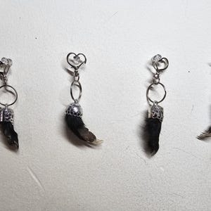May include: Four unique earrings featuring small animal paws. Each earring has a silver-colored metal clasp, a decorative metal cap, and a small paw with fur and claws. The clasps have heart and star designs.