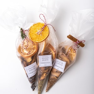 May include: Three clear cellophane bags filled with dried fruit and spices, tied with red and white twine. Each bag has a label that reads "Christmas Morning Simmer Pot", "Holiday Hearth Simmer Pot", and "Apple Pie Comfort Simmer Pot".