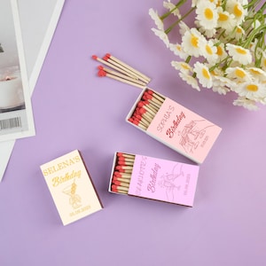 May include: Three matchboxes with custom birthday designs. One box is cream-coloured with gold text, and the other two are pink with white text. The matches have red tips. The text on the boxes reads "Selena's Birthday", "Sophia's Birthday", and "Charlotte's Birthday".