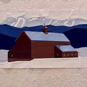 Op de afbeelding: Een textielkunstwerk dat een winterlandschap uitbeeldt. Een bruin gebouw met een met sneeuw bedekt dak staat voor donkerblauwe bergen en een witte, besneeuwde voorgrond. De lucht is lichtblauw.