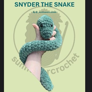 Peut inclure: Image d'un serpent en crochet vert d'eau nommé "Snyder". Le serpent est tenu dans une main, mettant en valeur son aspect doux et texturé. Le texte "SNYDER THE SNAKE" est affiché au-dessus du serpent, avec le nom du créateur en dessous.