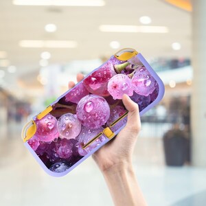 Könnte beinhalten: Handy-Schutzhülle mit Nahaufnahme von lila Trauben mit Wassertropfen. Die Hülle hat einen hellvioletten Rand mit gelben Akzenten. Die Trauben sind in verschiedenen Lila- und Rosatönen gehalten.
