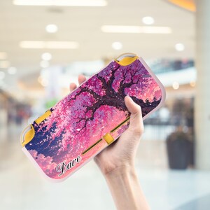 Può includere: Una custodia rosa e viola per Nintendo Switch con un'illustrazione panoramica di un albero in fiore. La custodia ha un nome personalizzato, "Dave", in corsivo. La custodia Switch ha dettagli gialli.