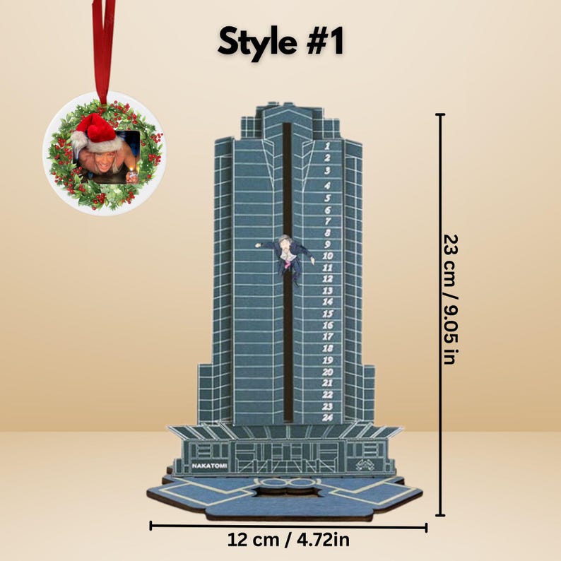 May include: A blue and gray skyscraper-shaped ornament with a figure hanging from it. The ornament is 9.05 inches tall and 4.72 inches wide. A smaller round ornament with a Santa hat is attached. The text "NAKATOMI" is visible.