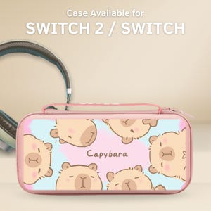 Puede incluir: Funda rosa para Switch 2 / Switch con diseño de carpincho. La funda tiene cierre de cremallera y un fondo azul claro y rosa. El texto "Case Available for SWITCH 2 / SWITCH" está en la parte superior. La palabra "Capybara" está escrita en la funda.