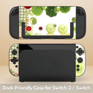 May include: A black Nintendo Switch console and dock with a decorative case featuring a whimsical design. The case has a white background with green apples, leaves, and cartoon characters. The text "Dock-Friendly Case for Switch 2 / Switch" is at the bottom.