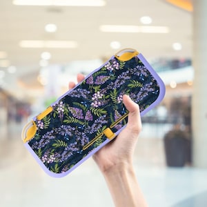 May include: A handheld gaming console case with a floral pattern. The case features a dark blue background with purple and white flowers and green leaves. The case has yellow accents and a light purple border.