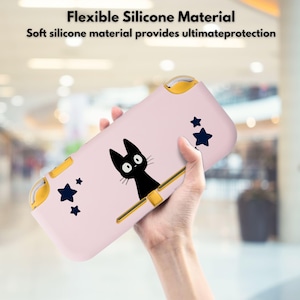 Puede incluir: Una funda de silicona rosa para consola de juegos portátil, con una ilustración de gato negro y estrellas azul marino. La funda tiene detalles dorados y el texto "Flexible Silicone Material" y "Soft silicone material provides ultimate protection".