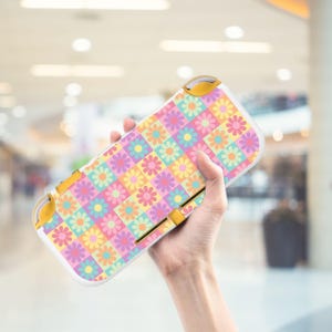 Può includere: Una custodia per console di gioco portatile con un motivo floreale colorato. La custodia presenta una griglia di quadrati dai colori pastello, ciascuno contenente una margherita. La custodia ha dettagli gialli e un bordo bianco.