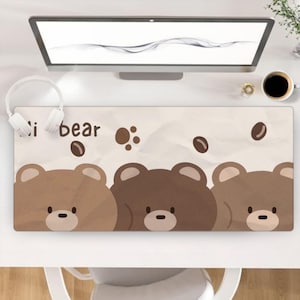 以下が含まれることがあります： ベージュ色の長方形デスクマット。茶色系のクマの顔が3つ描かれています。「i bear」の文字とコーヒー豆のイラストもプリントされています。デスクの表面を保護するように設計されています。
