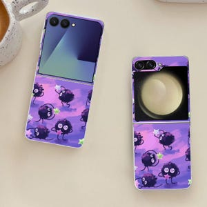 May include: Two open purple flip phones with a cartoon design. The design features black, fluffy creatures holding stars against a purple and pink background. One phone displays a gradient screen, the other a planet.