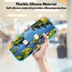 Può includere: Una custodia in silicone blu e gialla per un dispositivo di gioco. La custodia presenta una serena scena di stagno con illustrazioni di gatti bianchi su ninfee. Il testo in alto recita "Flexible Silicone Material".