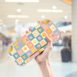 May include: A pastel-coloured Nintendo Switch Lite case with a floral pattern. The case has a checkerboard design with squares of blue, peach, and yellow, each adorned with a different flower. The case has yellow buttons and a light pink border.