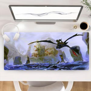 Könnte beinhalten: Rechteckige Mauspad mit einer Fantasy-Szene, die einen Drachen zeigt, der über Wasser auf ein Schloss zufliegt. Das Kunstwerk verwendet Farbtöne von Blau, Grau und Schwarz auf weißem Hintergrund. Das Pad liegt auf einem weißen Schreibtisch mit Monitor, Kopfhörern und einer Kaffeetasse.