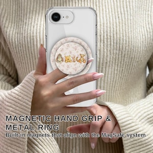 May include: A clear phone case with a pop-up grip featuring Winnie the Pooh characters. The grip has a floral background. The phone is held by a person wearing a beige sweater. The text on the image says "MAGNETIC HAND GRIP & METAL RING".