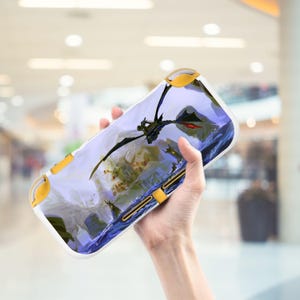 May include: White and yellow handheld gaming console case featuring a fantasy landscape with a black dragon. The case has yellow accents on the top and bottom. The dragon has red accents.