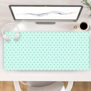 Puede incluir: Una alfombrilla de escritorio rectangular con un fondo verde menta claro y un patrón repetitivo de pequeños puntos de color verde azulado oscuro. La alfombrilla está colocada sobre un escritorio blanco bajo un monitor y auriculares blancos.