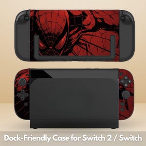 May include: A black gaming console dock and handheld device featuring a red and black graphic skin of a masked superhero with a web pattern. The console has black buttons, joysticks, and a screen. The text Dock-Friendly Case for Switch 2 / Switch is visible.