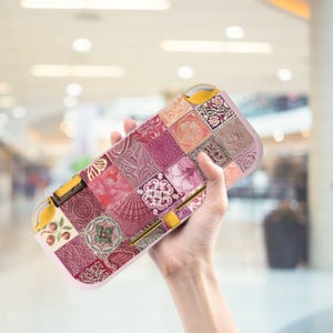 Könnte beinhalten: Eine rosa-goldene Nintendo Switch-Hülle mit einem Patchwork-Design aus gemusterten Fliesen in Rosa, Rot und Braun. Die Hülle hat gelbe Akzente und eine glatte, abgerundete Form und bietet Schutz und Stil.