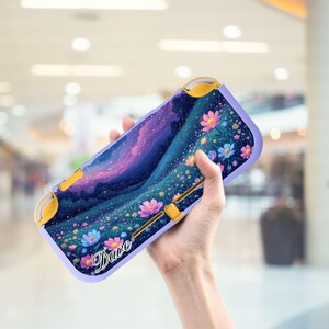 Puede incluir: Una funda de consola de juegos de color lavanda con un diseño floral y paisajístico vibrante. La obra de arte representa un cielo nocturno estrellado, un campo de flores coloridas y el nombre "Dave" en cursiva. La funda tiene detalles amarillos.
