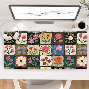 Peut inclure: Un tapis de bureau rectangulaire composé d'une grille de carrés, chacun présentant un motif floral brodé unique dans des tons variés de rose, jaune, rouge, blanc et violet sur des fonds vert foncé, bleu et crème.