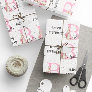 May include: Pink and white wrapping paper featuring a bunny and the letter B. The paper reads "Happy Birthday" and "Bella".