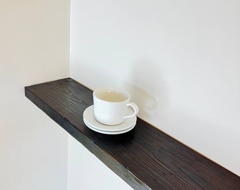 May include: A white ceramic teacup and saucer on a dark brown wooden shelf.