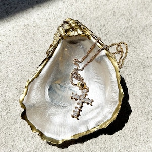 May include: A gold-colored oyster shell dish with a gold chain necklace and a cross pendant with clear stones.