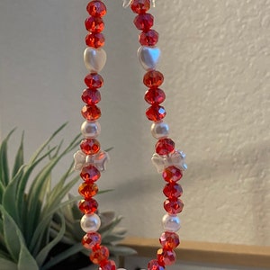May include: A red and white beaded charm with a Hello Kitty charm hanging from it. The beads are alternating red and white, and there are two white bows on the charm.