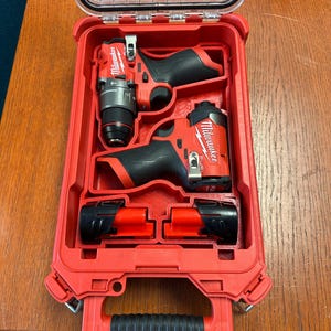 May include: A red Milwaukee power tool kit with a clear lid. The kit contains two red and black power drills and two red battery packs. The tools are neatly organized inside the red case.