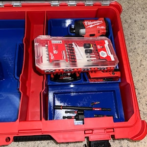 May include: A red and blue tool box with a Milwaukee FUEL drill and a clear plastic case of 25 screwdriver bits inside.